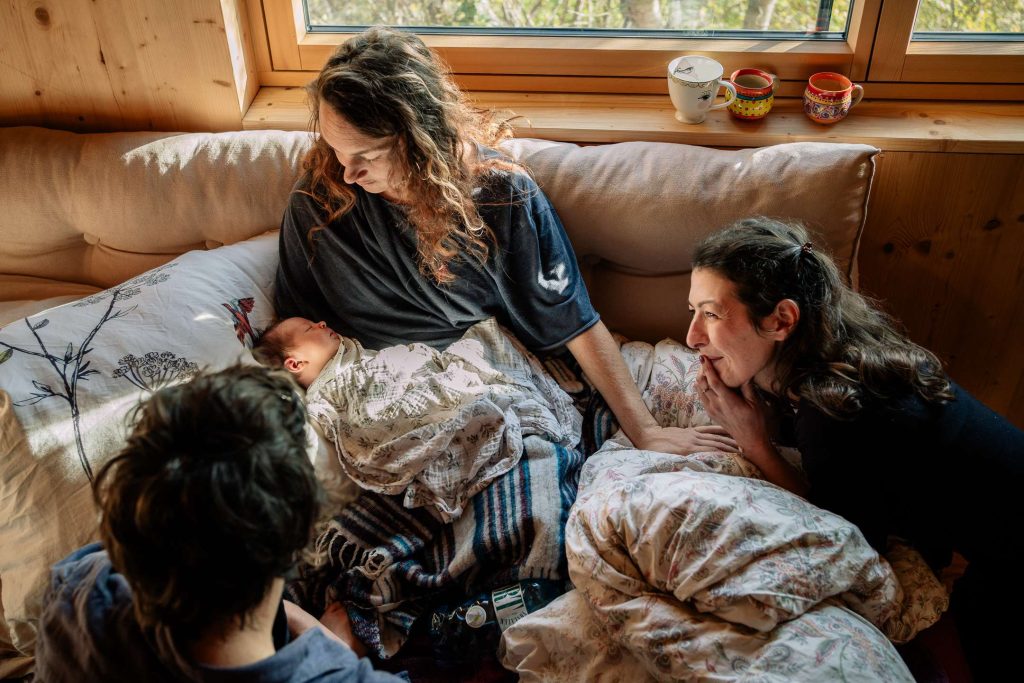 Doula mit Mamas und frisch geborenem Baby im Wochenbett und das natürliche Licht lässt alle strahlen
