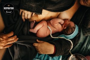Frisch Geborenes Baby saugt an der Brust und liegt dabei nackt auf Mutters Bauch und die Nabelschnur verbindet noch zur Plazenta