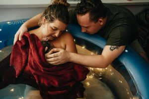 Vater und Mutter bestaunen das erste Mal ihr neugeborenes Baby das gerade zuhause im Geburtspool zur Welt gekommen ist.