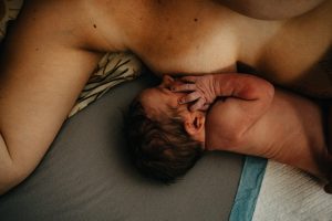 Frisch geborenes Baby stillt an der Brust mit viel Haut nach Hausgeburt