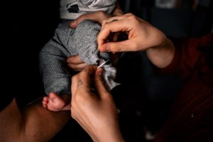 zwei Hände ziehen dem neugeborenen Baby die graue Hose an